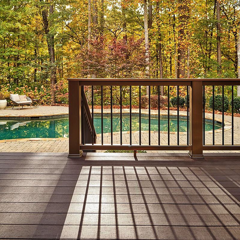 Wooden deck overlooking a turquoise pool and autumn trees, with railing shadows across the floor.