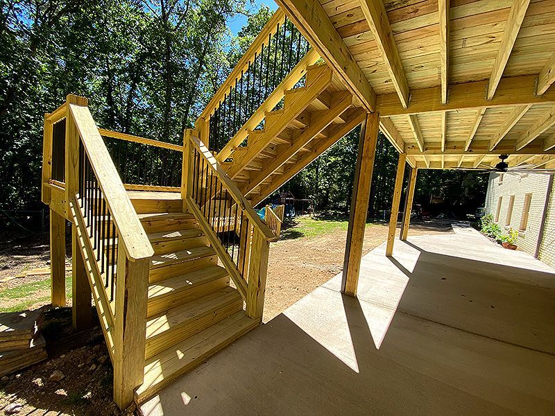Wooden outdoor stairs and elevated deck under construction beside a concrete patio in a sunny yard