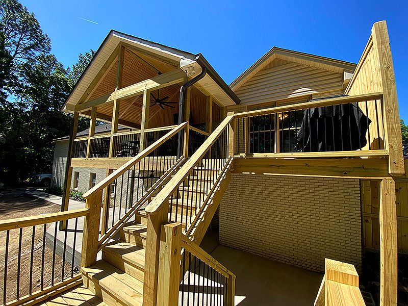 Two-story wooden house with a large front staircase under construction in sunny daylight