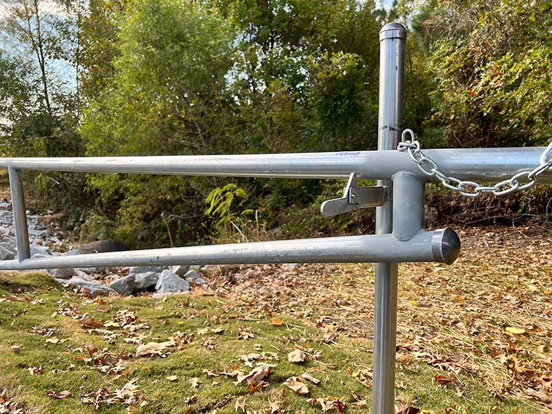 Metal farm gate with horizontal rails in a grassy yard beside trees and autumn leaves