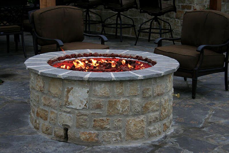 Stone outdoor fire pit with glowing embers on a patio, surrounded by chairs