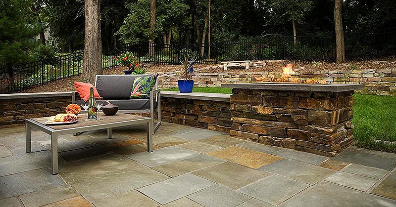 Patio with metal lounge chair, potted plants, and stone retaining wall in a wooded yard