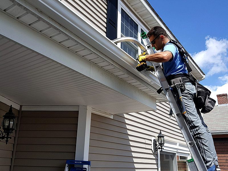 Worker using a power drill on a house gutter from a ladder