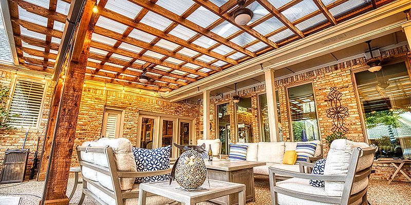 Sunlit rustic lounge with stone walls, white sofas, and a wooden pergola ceiling