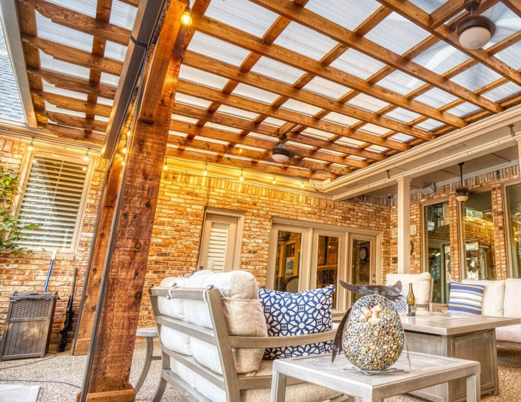 Covered patio with wicker seating, wood beams, and a patterned tile ceiling, overlooking a cozy outdoor lounge.