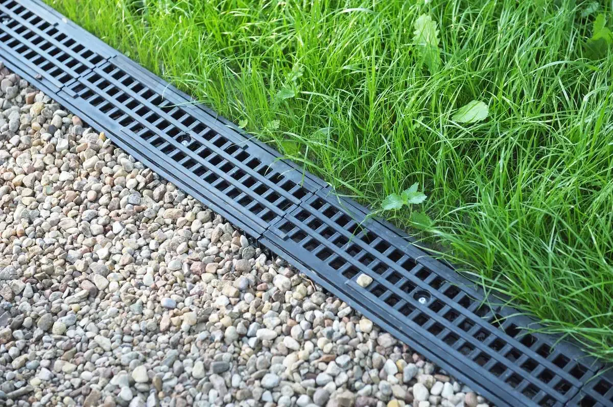 Black drainage grate between gravel path and green grass