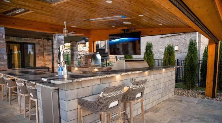 Covered patio outdoor kitchen featuring a built-in grill station, dining set, and stone fireplace