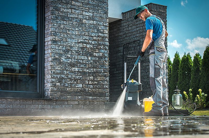 Worker pressure washing a brick house patio with a spray wand and water spray