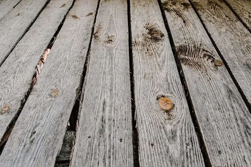 Weathered gray wooden deck boards with scattered leaves and small dark stains