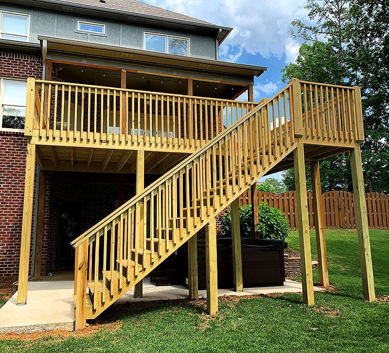Raised wooden backyard deck with stairs, railing, and support posts beside a brick house