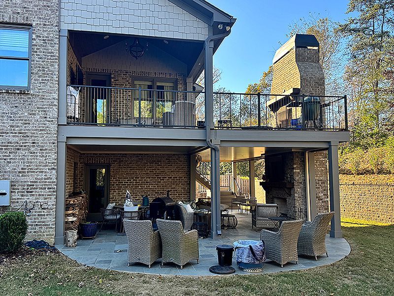 Back patio with wicker seating beneath an upper balcony on a brick house