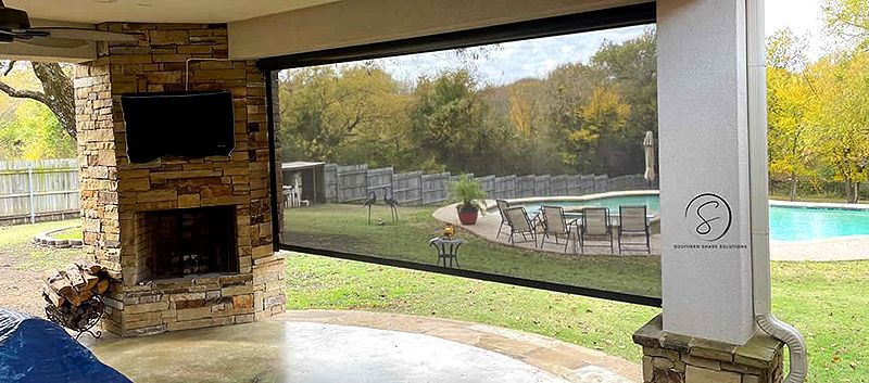 Covered patio with stone fireplace, lawn, and a pool in the background at sunset