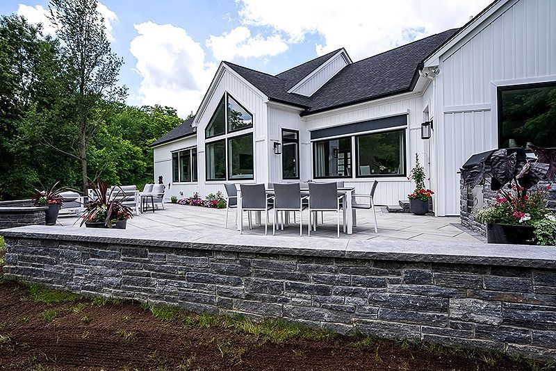 Modern white house with large patio, outdoor dining table, and landscaped garden under a partly cloudy sky