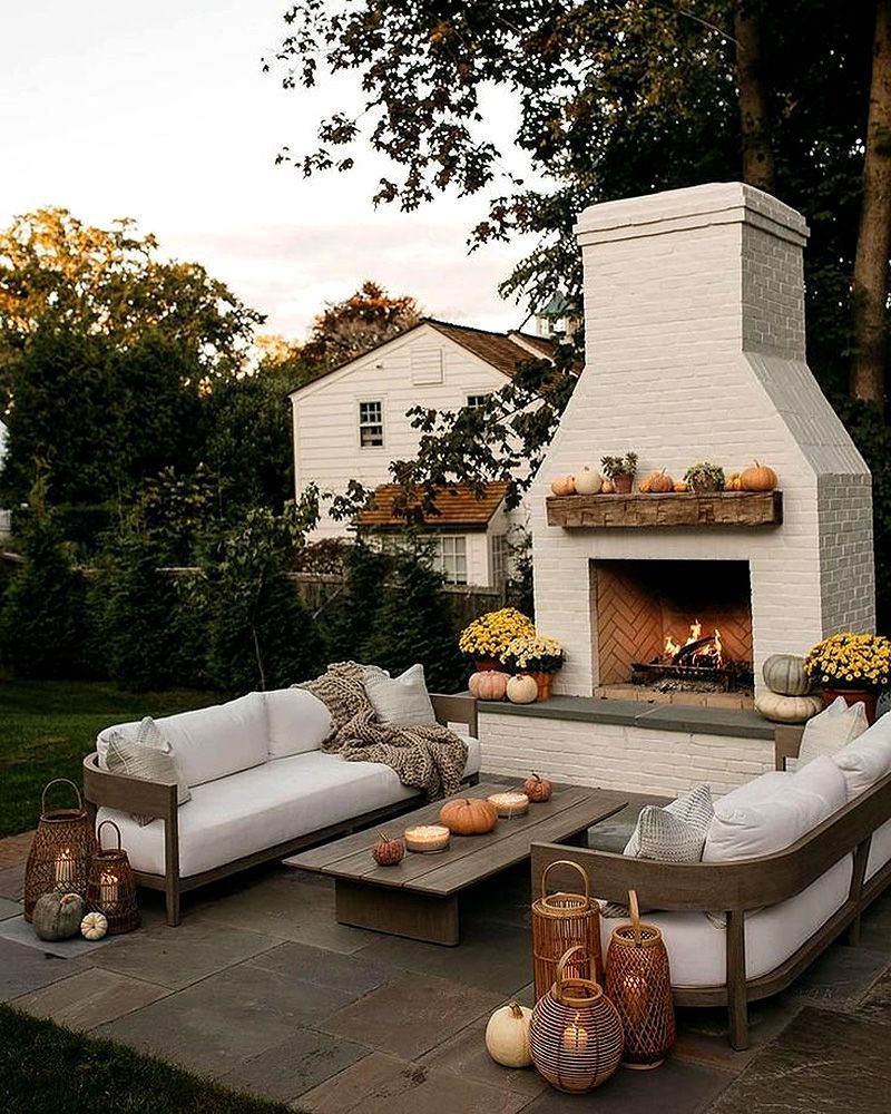 Outdoor patio with white fireplace, cushioned seating, coffee table, and autumn decor at dusk