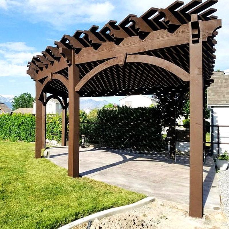 Brown wooden pergola over a concrete patio beside a green lawn under a blue sky