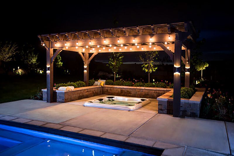 Lit wooden pergola over a hot tub beside a glowing pool at night