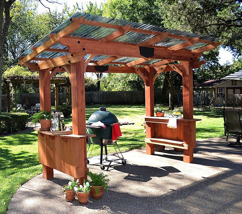 Wooden outdoor pergola with a built-in grill and counter in a sunny backyard garden