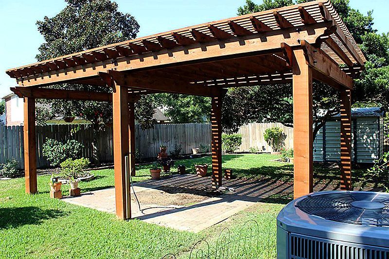 Wooden backyard pergola with slatted roof, built over a grassy patio beside an air conditioner.