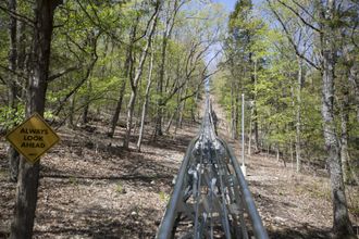 Coaster track heading uphill through wooded terrain with caution signage