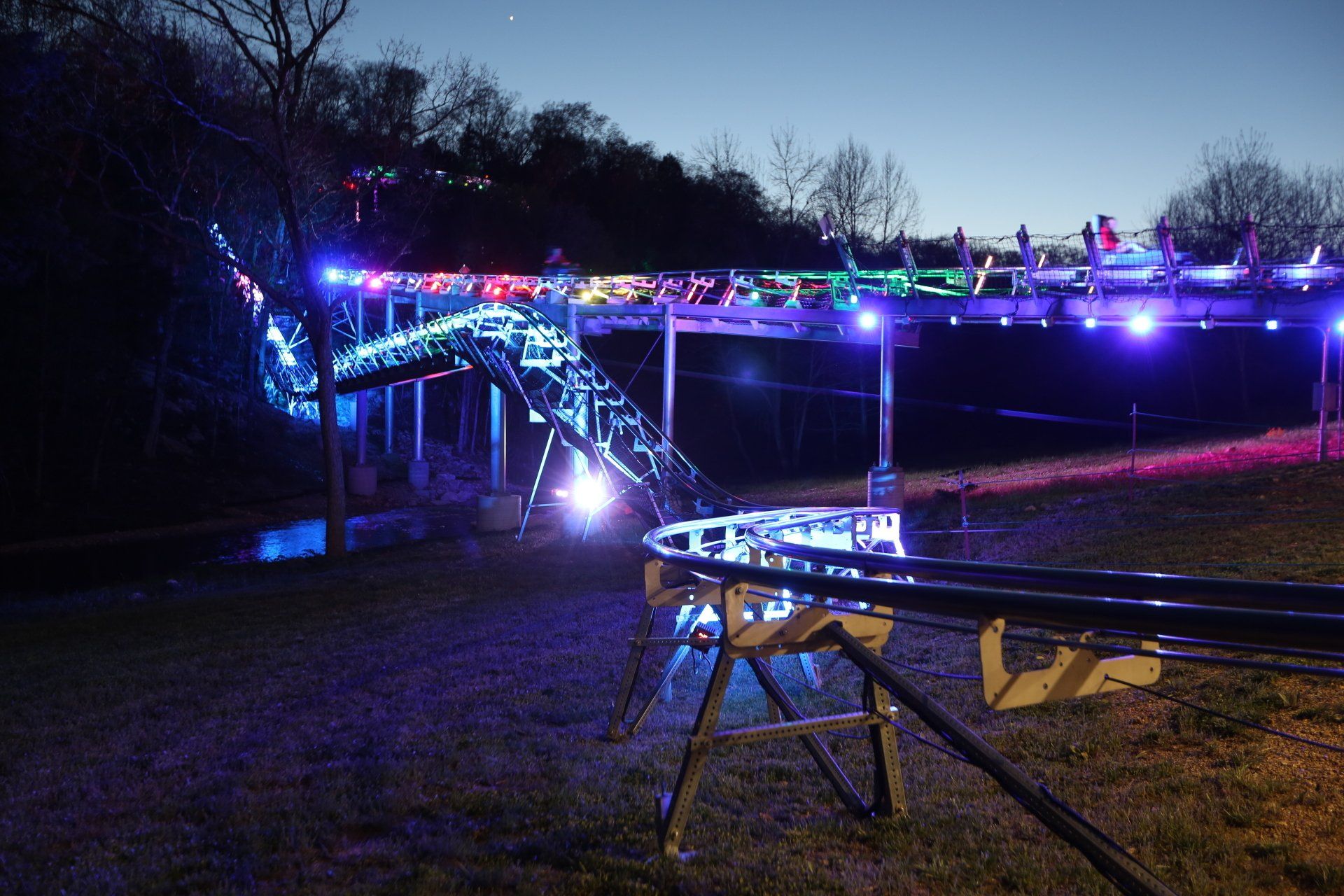 Mountain coaster track lit with vibrant purple, pink, and blue lights for a nighttime ride experience