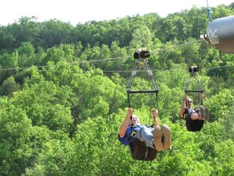 People riding a chairlift above a lush green canopy of trees