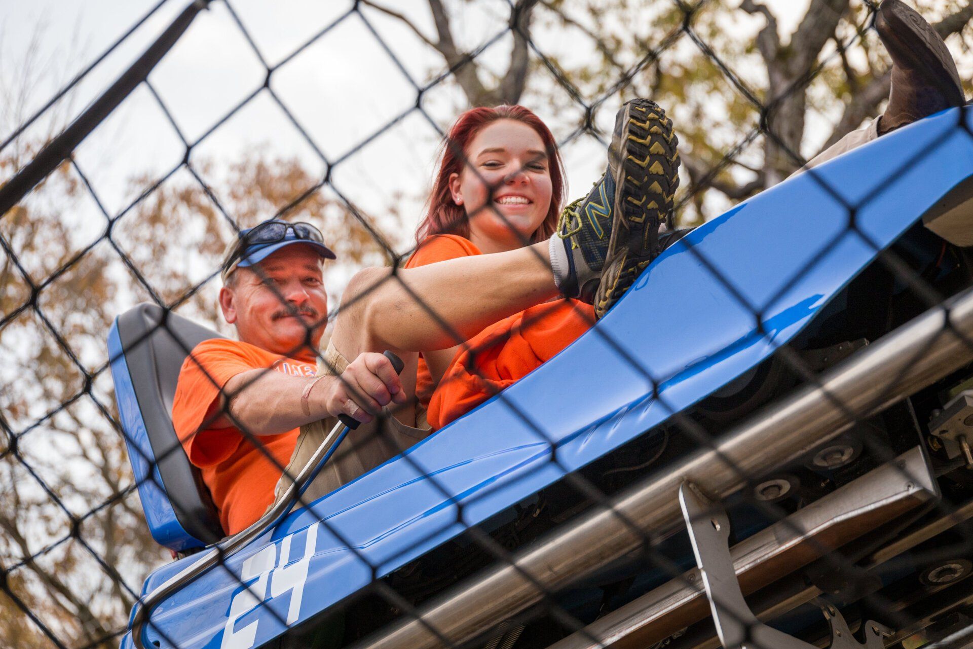 Two smiling riders on a mountain coaster enclosed by mesh fencing