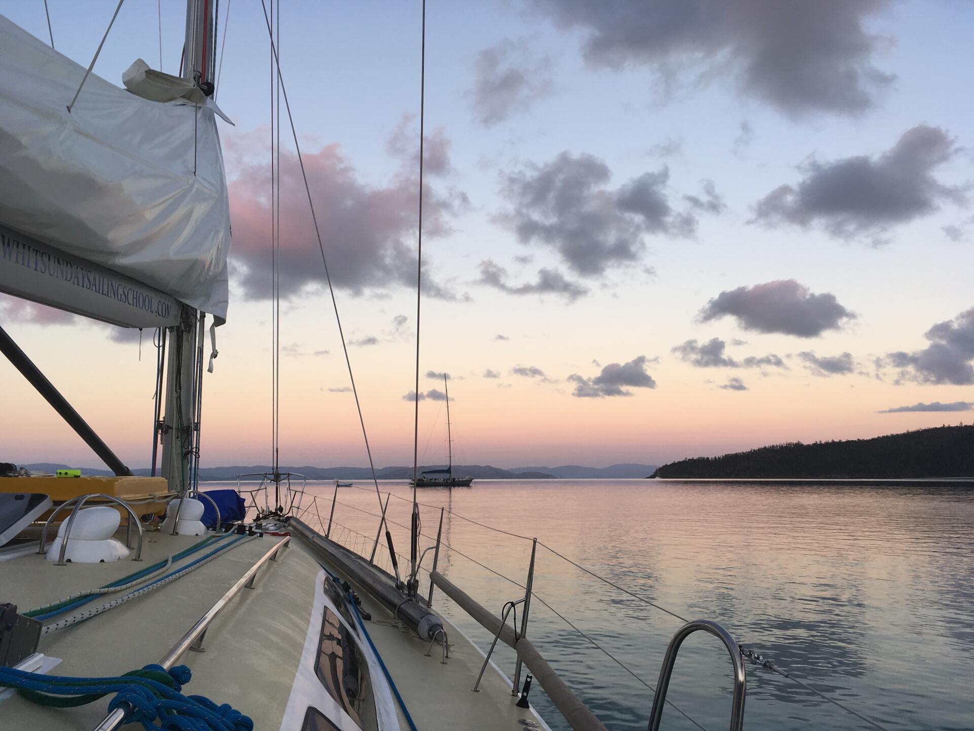 View from a sailboat deck at dusk, overlooking a calm bay with soft pastel skies