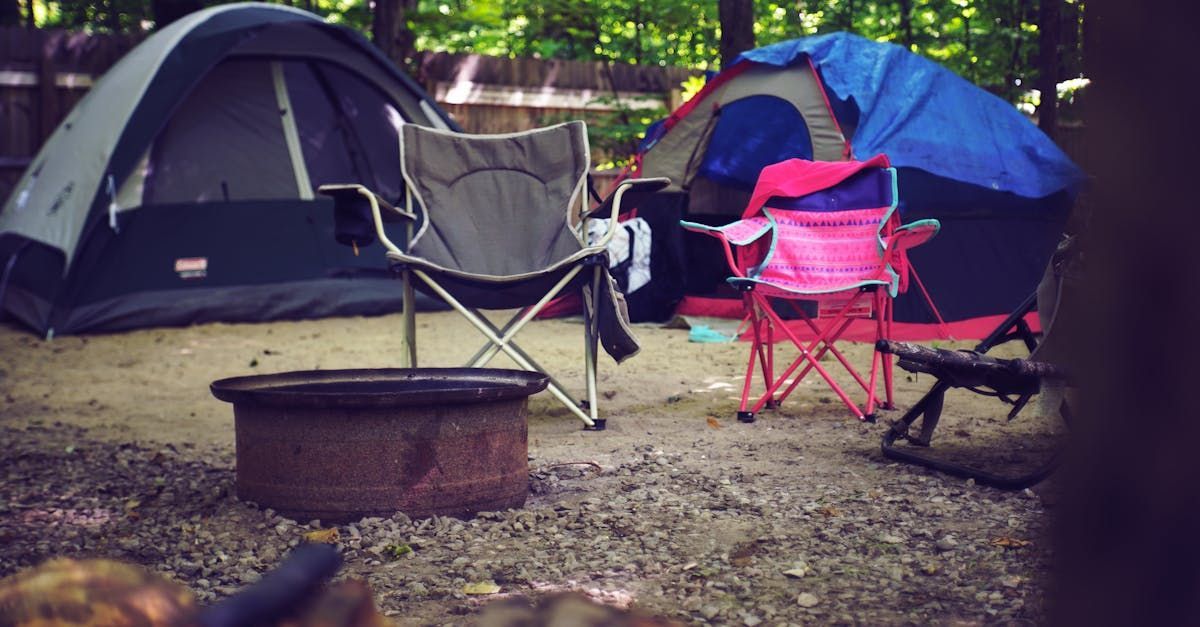 Tents and camping chairs set up around a fire ring at a wooded campsite.