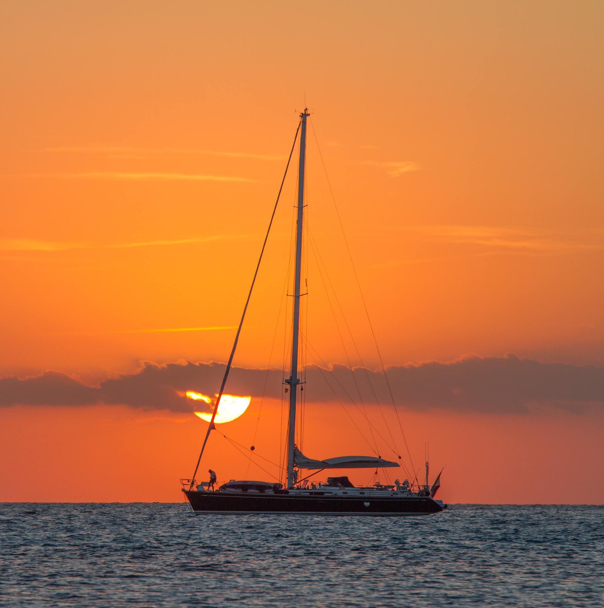 Silhouette of a sailboat on calm water during a vibrant orange sunset