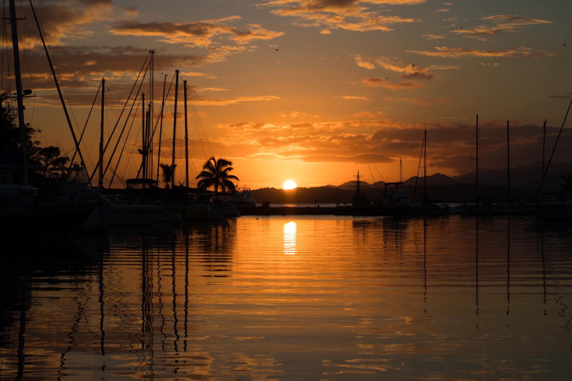 Boats docked at a marina with a glowing orange sunset reflecting on the water