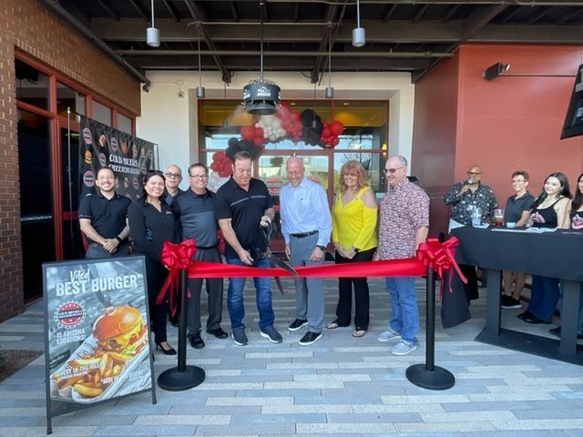 A group of people are standing in front of a restaurant cutting a red ribbon.
