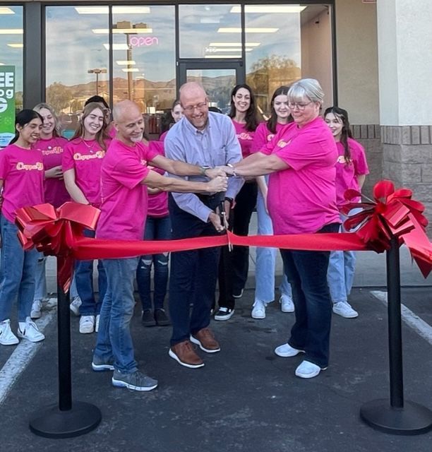 A group of people in pink shirts are cutting a red ribbon
