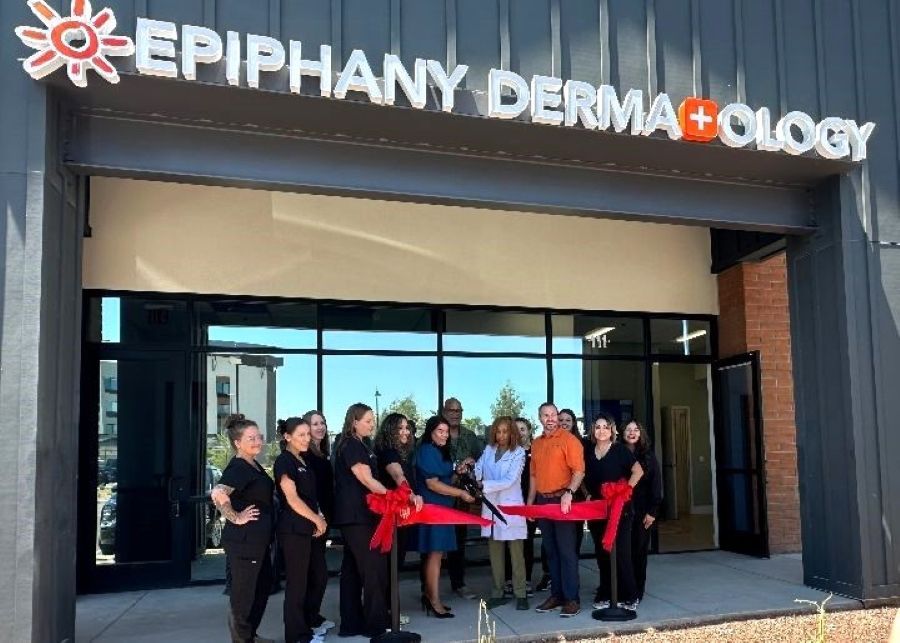 A group of people are cutting a red ribbon in front of epiphany derma ology