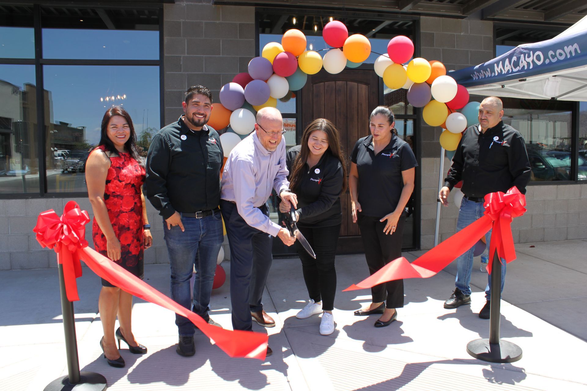 A group of people are cutting a red ribbon in front of a building