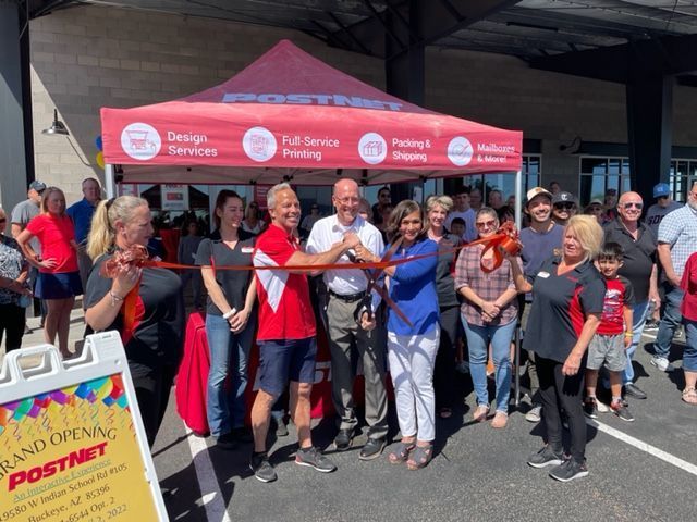 A group of people are standing under a red tent cutting a red ribbon.