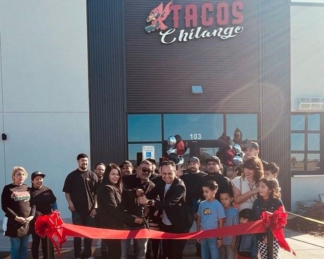 A group of people are cutting a red ribbon in front of a tacos chiliange restaurant