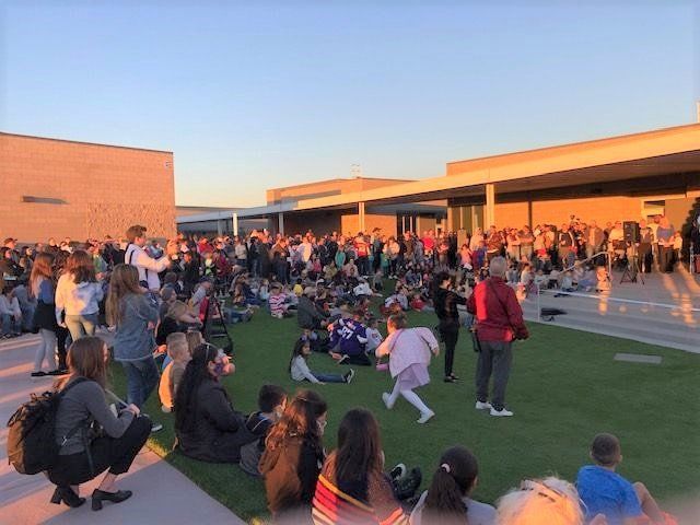 A large group of people are sitting on the grass in front of a building.