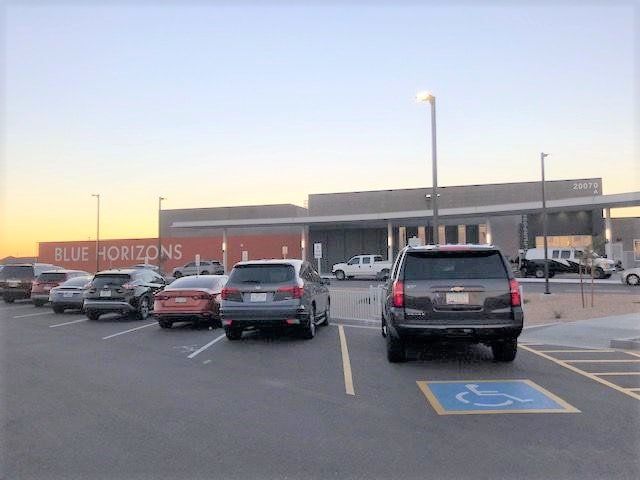 A row of cars are parked in a parking lot in front of a building that says blue horizons.