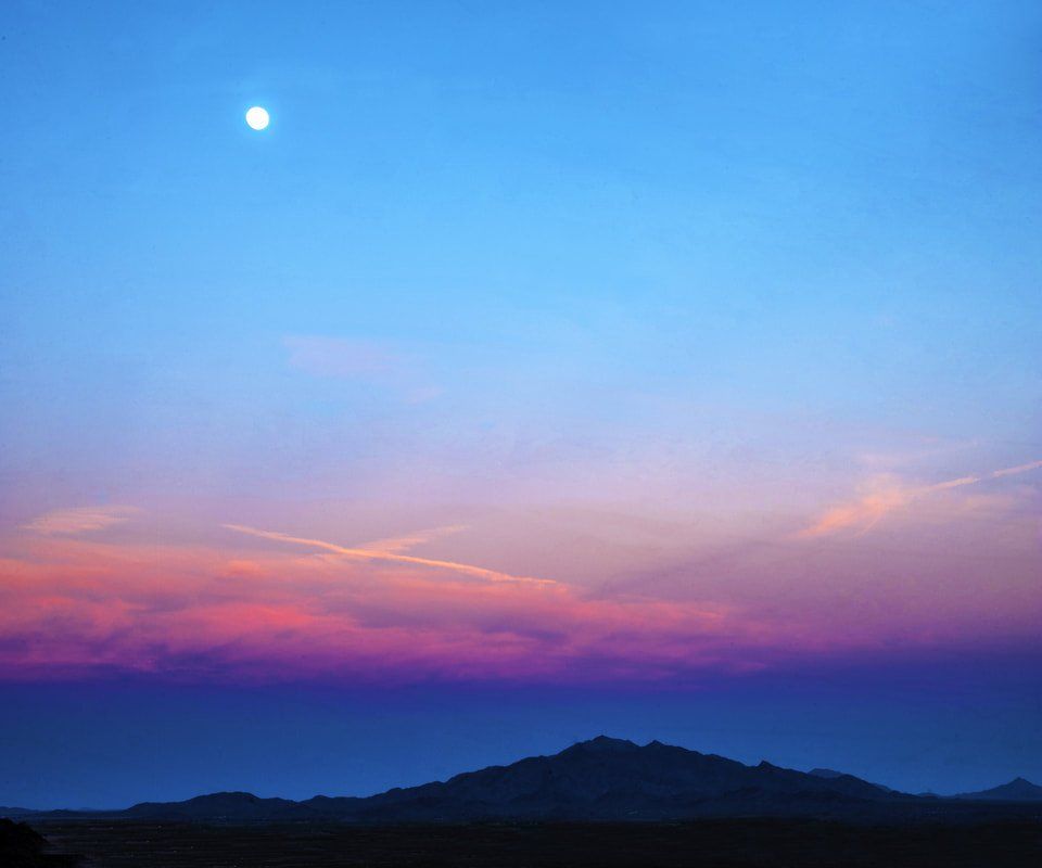 The moon is rising over the mountains at sunset.