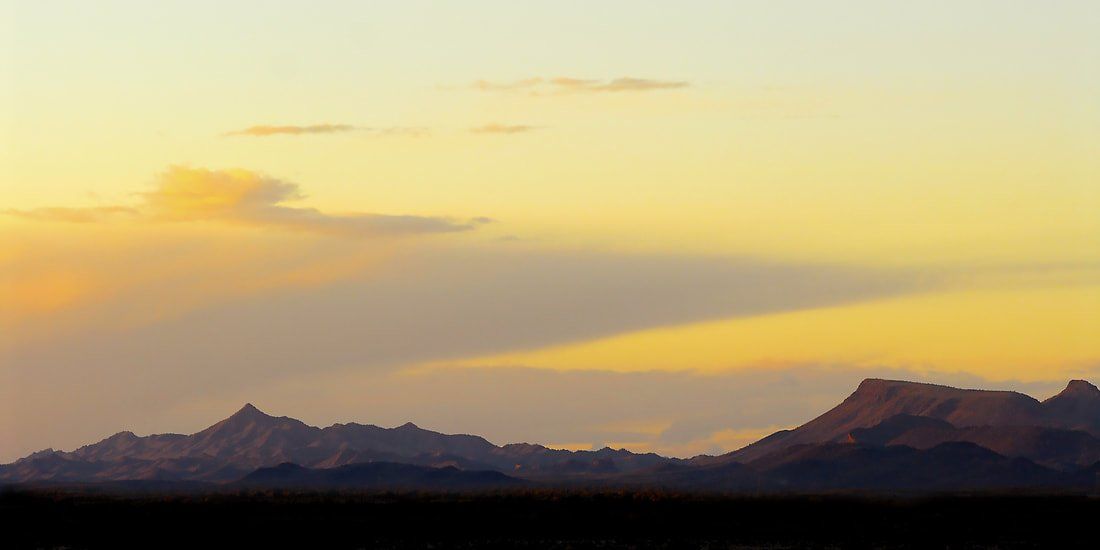 A sunset over a mountain range with a few clouds in the sky