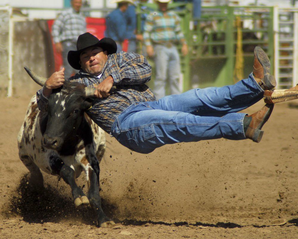 A man in a cowboy hat is being pulled by a bull