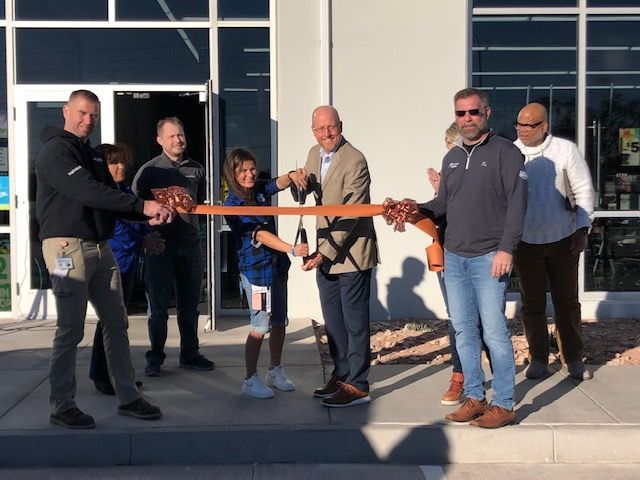 A group of people are cutting a ribbon in front of a building.
