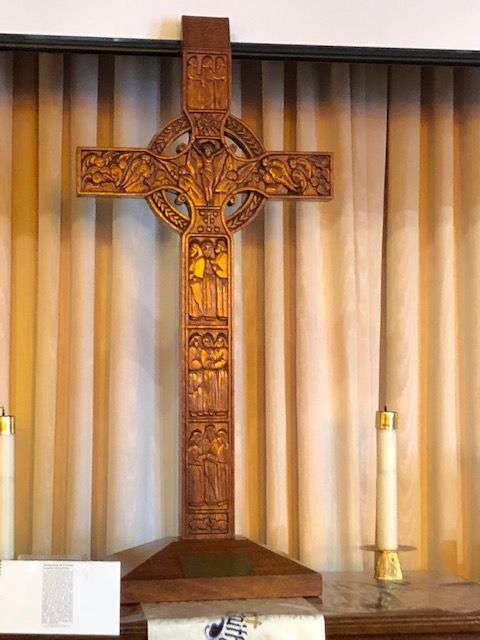 A wooden cross is sitting on a table in front of a window.