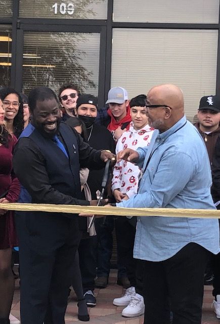 Two men are cutting a ribbon in front of a crowd of people.