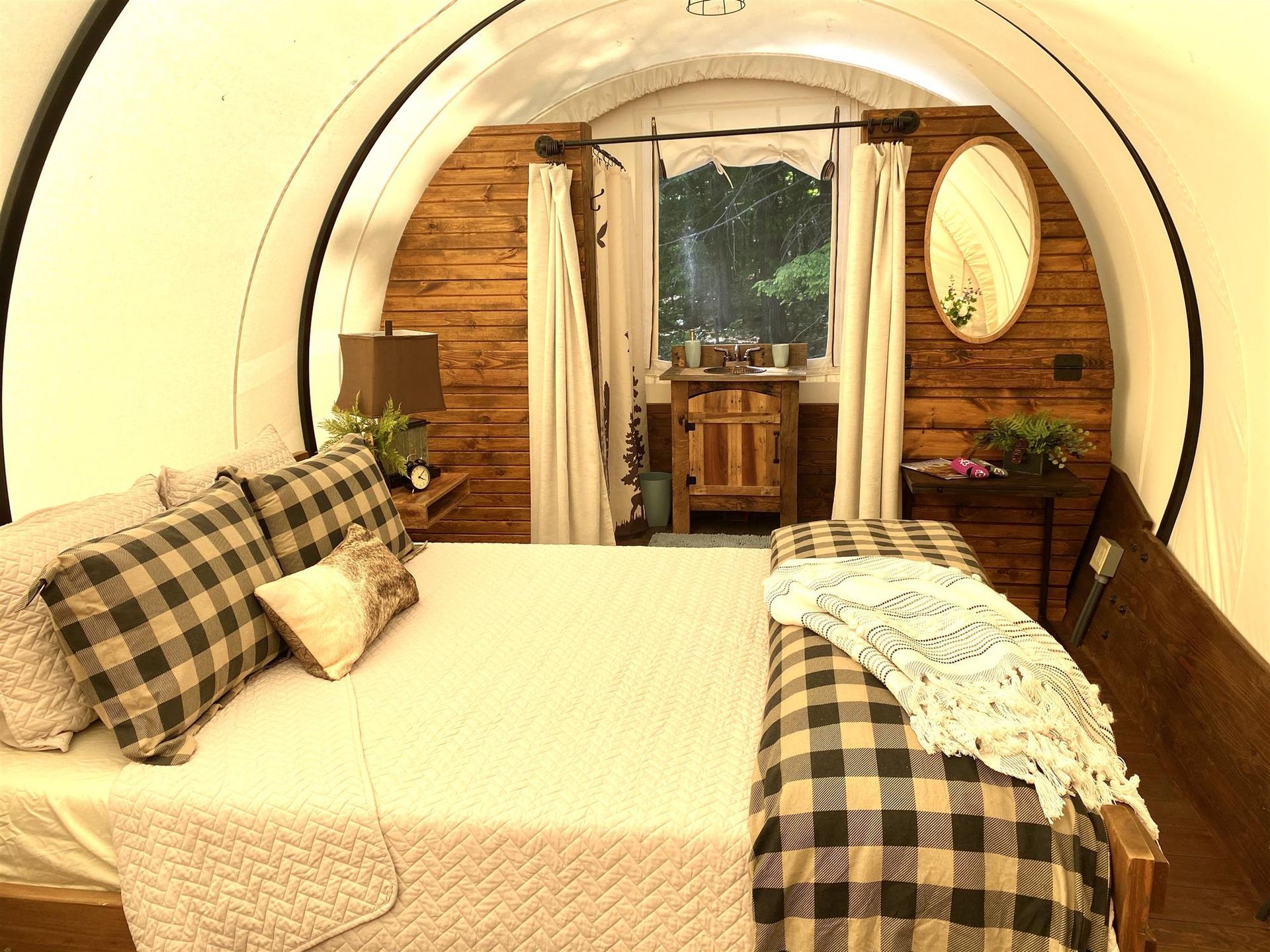 Cozy bedroom in a covered wagon, featuring a bed with plaid pillows, wooden walls, a window, and a bench.