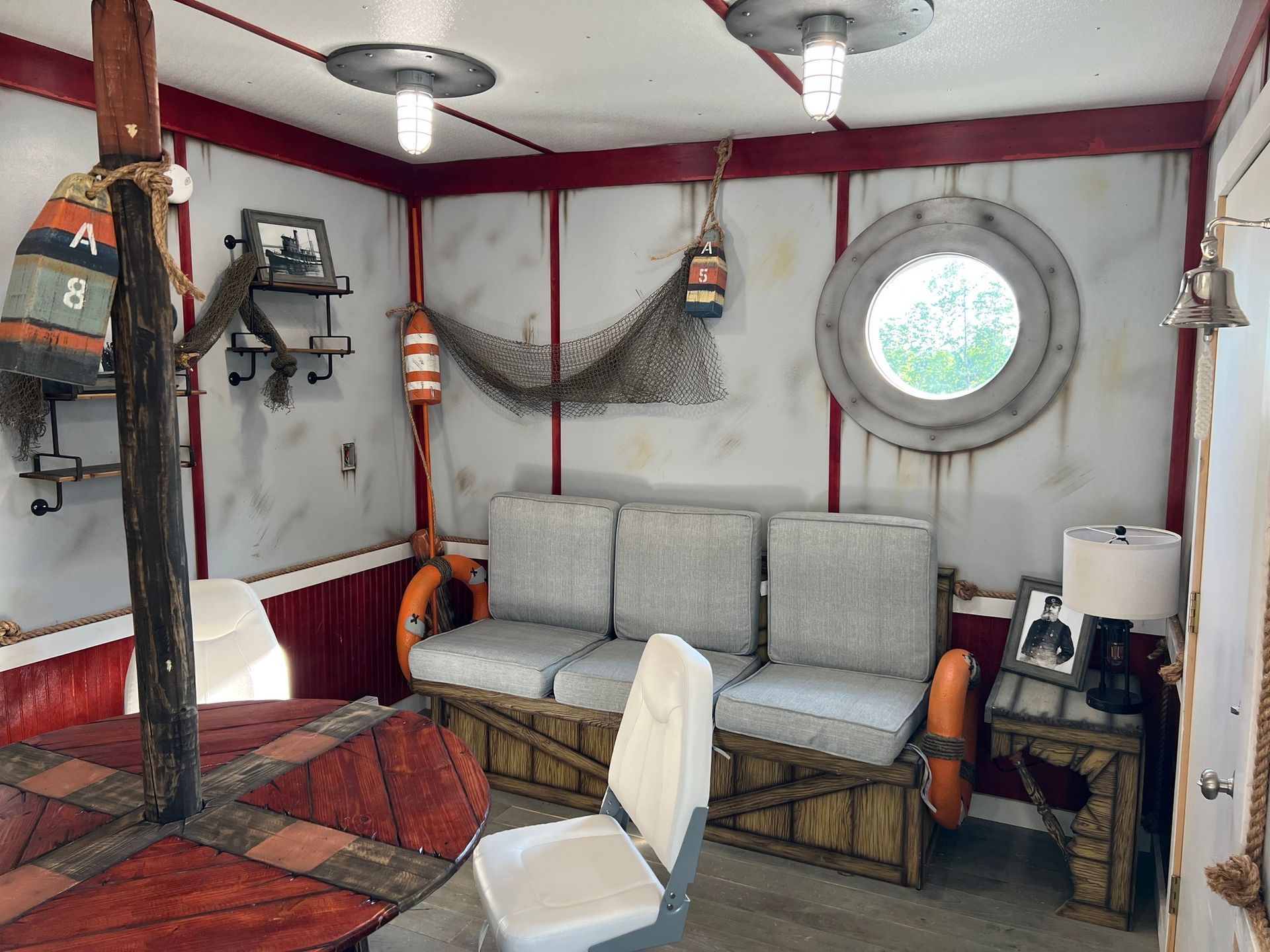 Nautical-themed room with wood paneling, porthole, sofa, life preservers, fishing net, and ship décor.