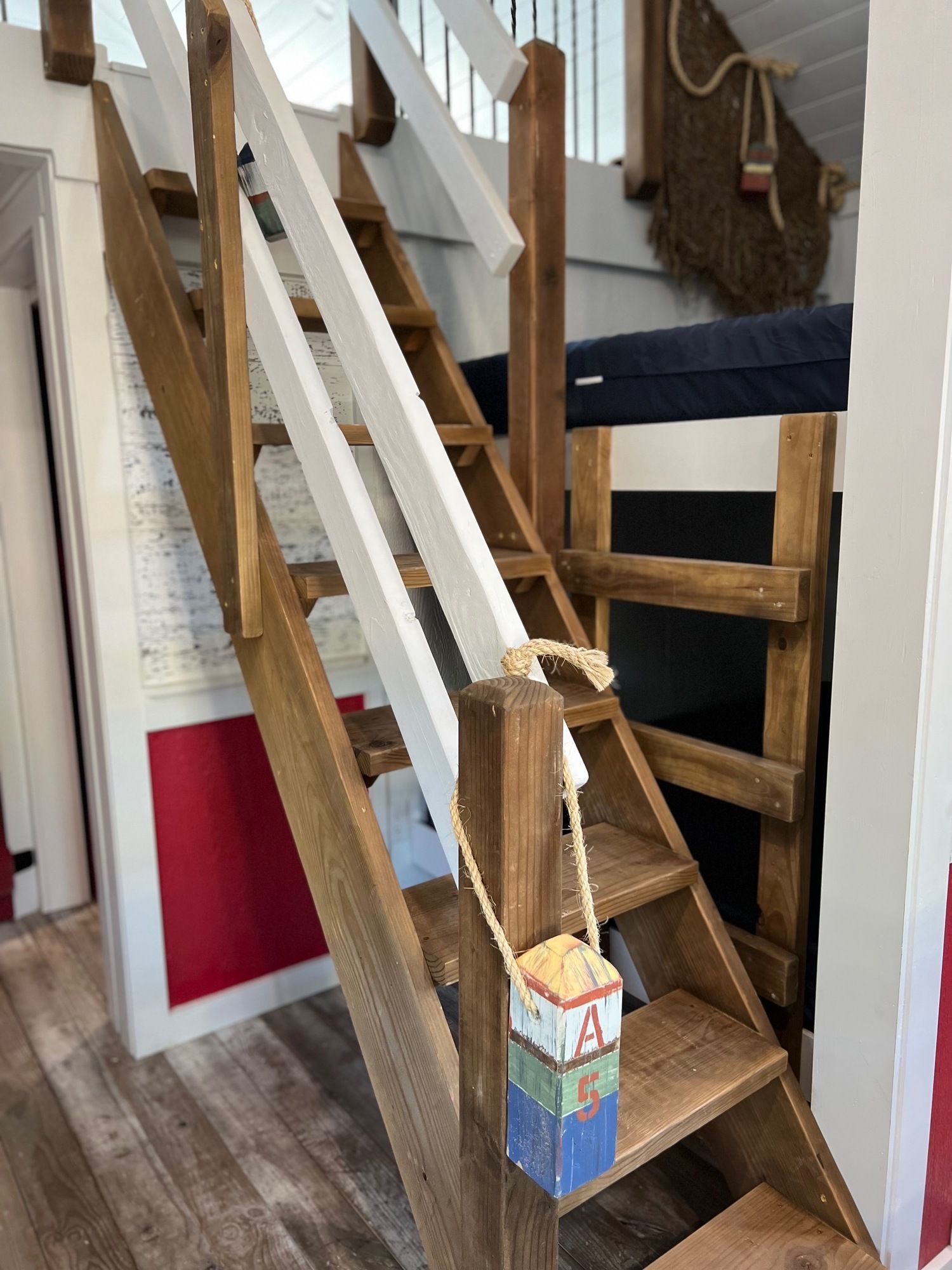 Wooden staircase with white railing leading to a bunk bed, decorated with nautical-themed items.