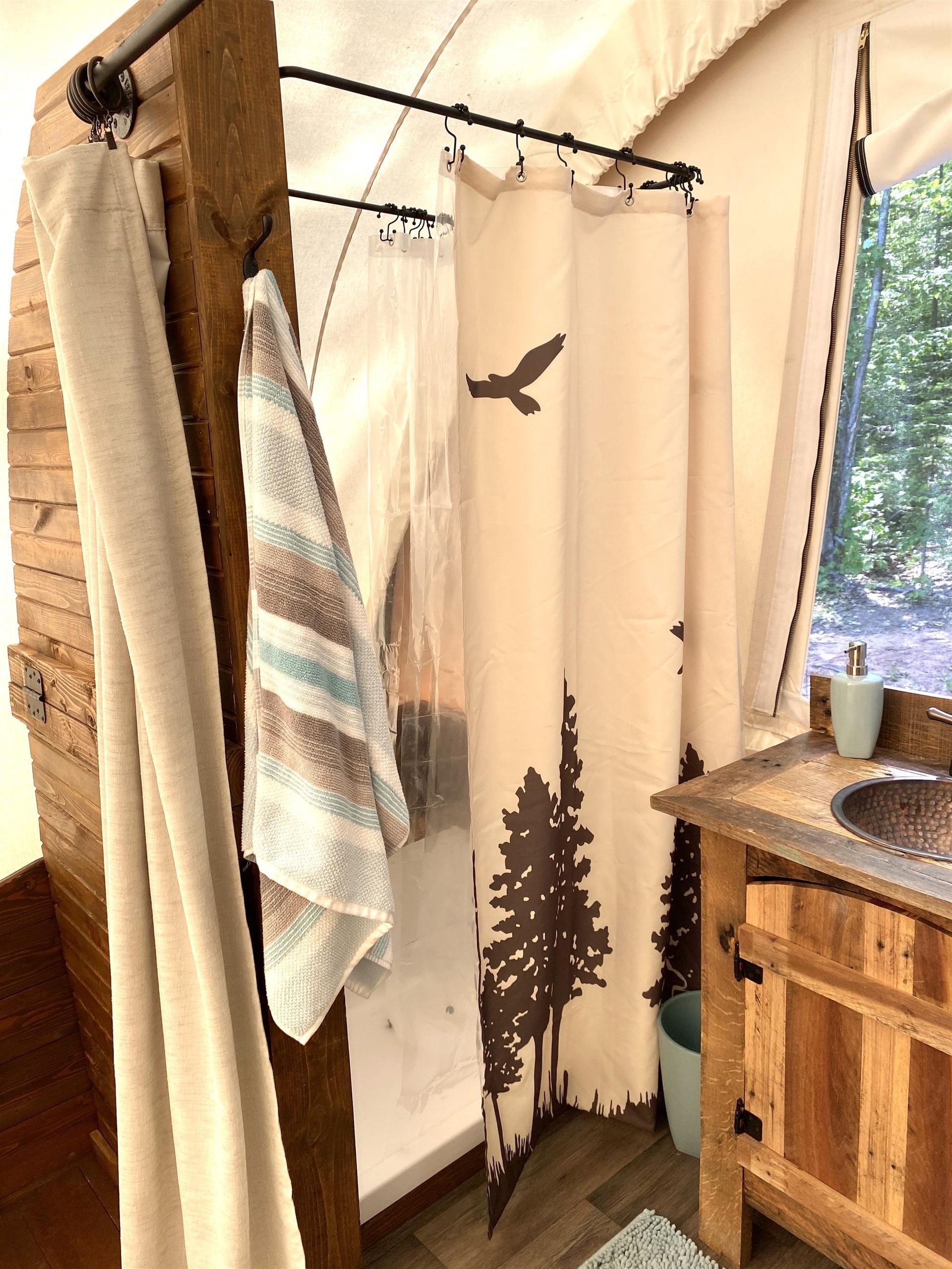 Outdoor shower with a forest-themed shower curtain, towel, and wooden vanity.