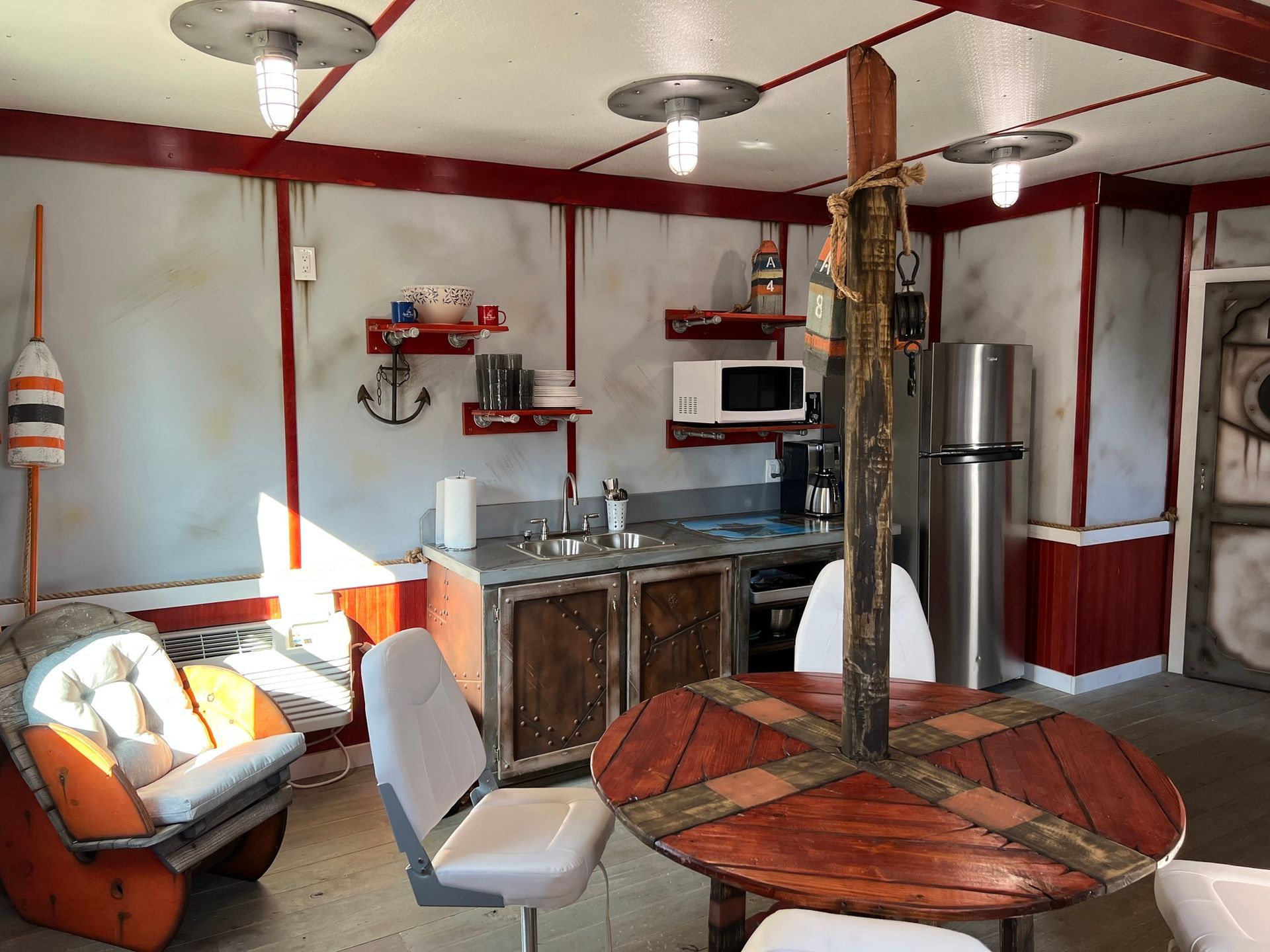 Small kitchen with nautical decor; round table, fridge, chair, sink, and microwave.