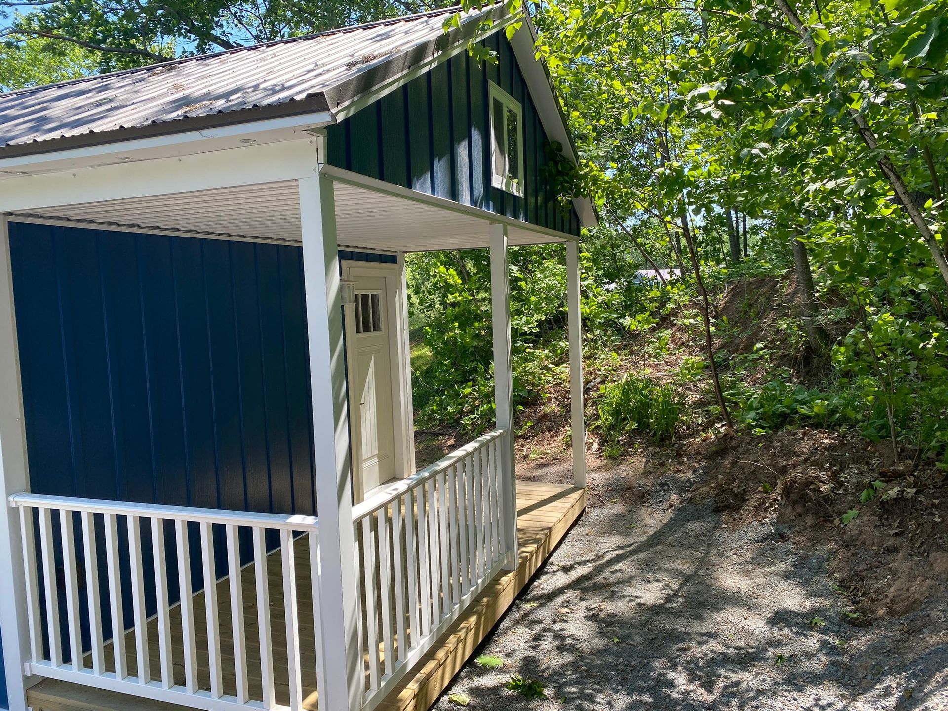 Blue cabin with white trim and porch, nestled in trees.